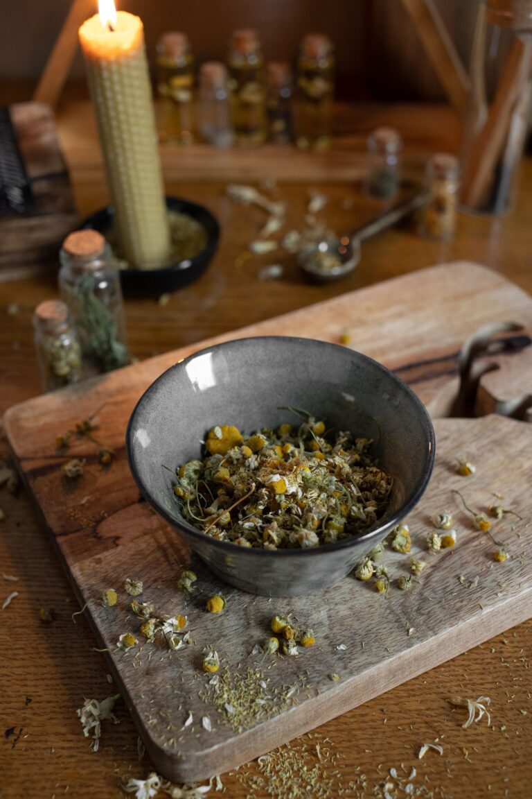 Tigela com flores de camomila secas sobre tábua de madeira rústica, com potes de ervas ao fundo