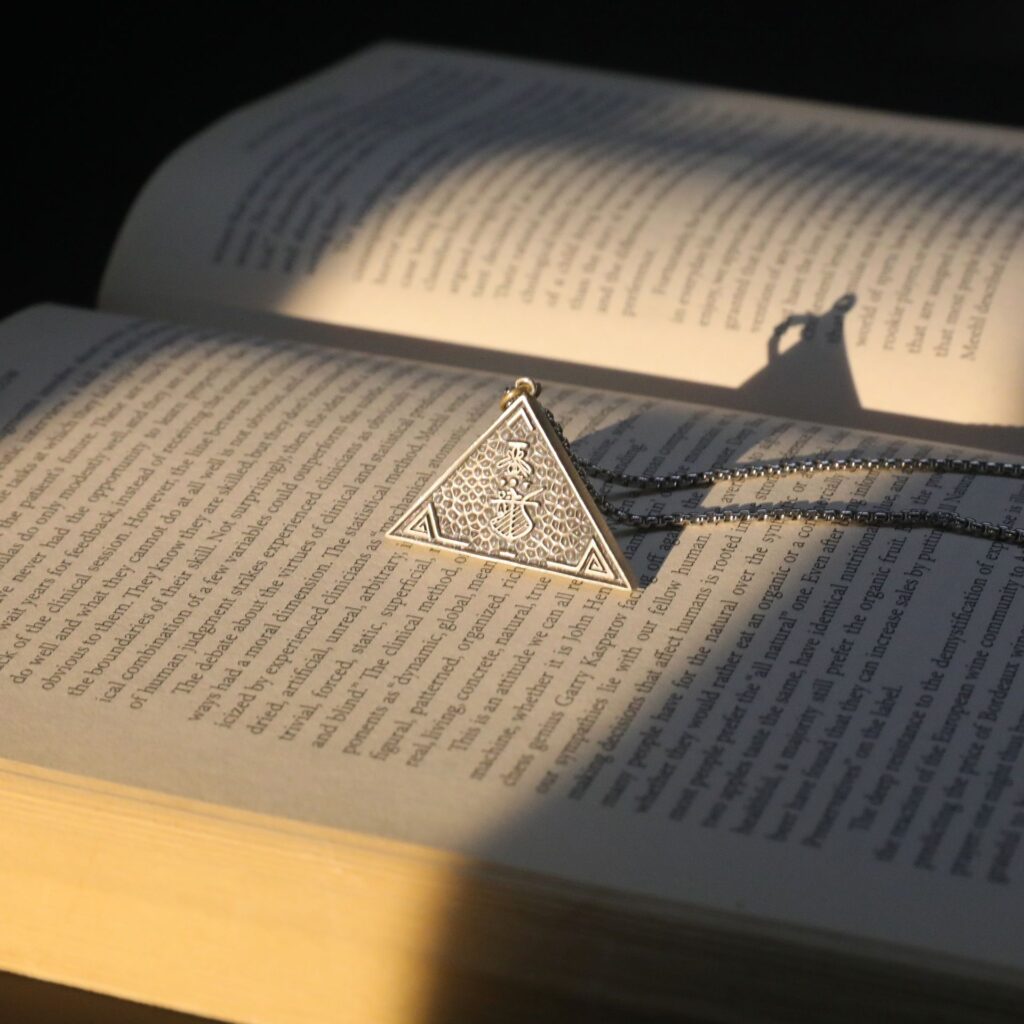 Medalha triangular hermética sobre livro aberto — as 7 leis herméticas do Kybalion