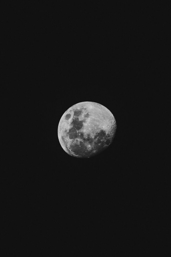 Lua quase cheia fotografada em close contra céu noturno completamente escuro, revelando crateras e superfície lunar em detalhes