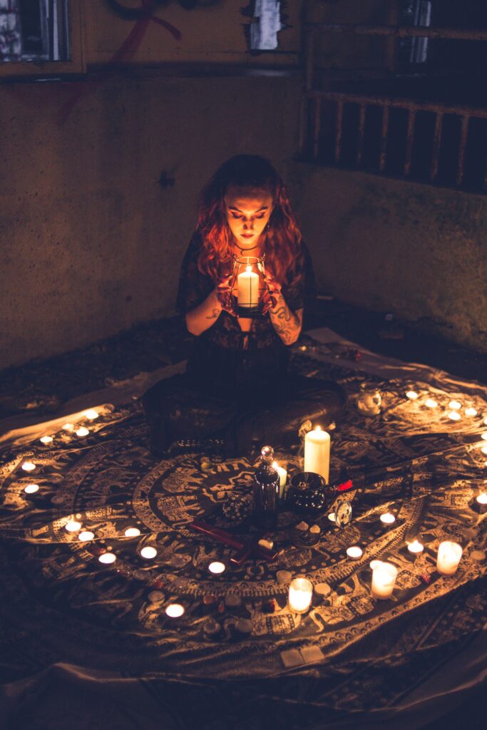 Mulher sentada em círculo mágico formado por velas acesas, segurando uma vela enquanto realiza ritual em ambiente escuro
