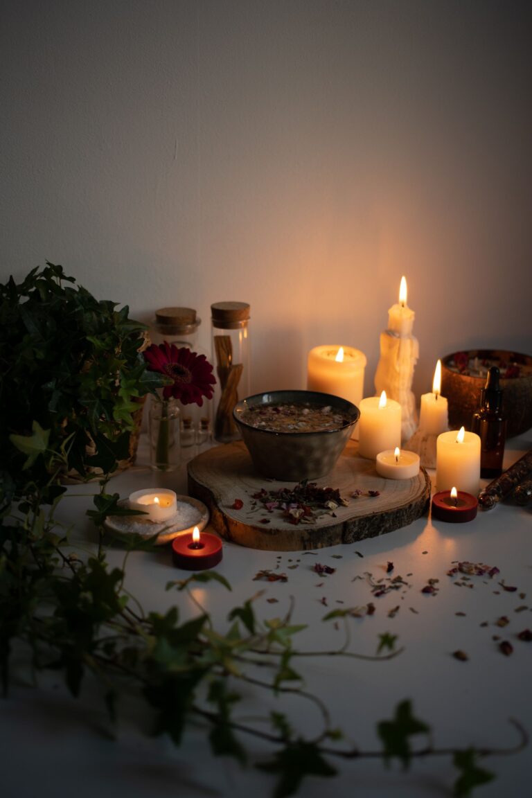 Altar de magia popular com tigela de água e ervas, velas acesas, hera e flores ao redor