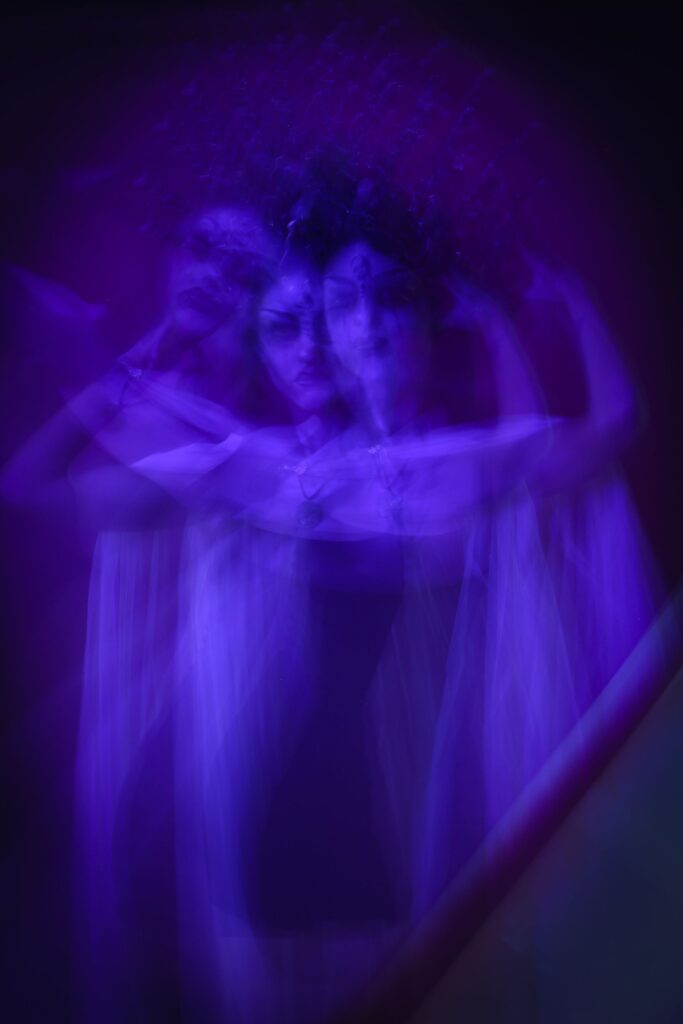 Dupla exposição de silhueta em tons violeta com braços erguidos, criando efeito etéreo e translúcido de desdobramento espiritual