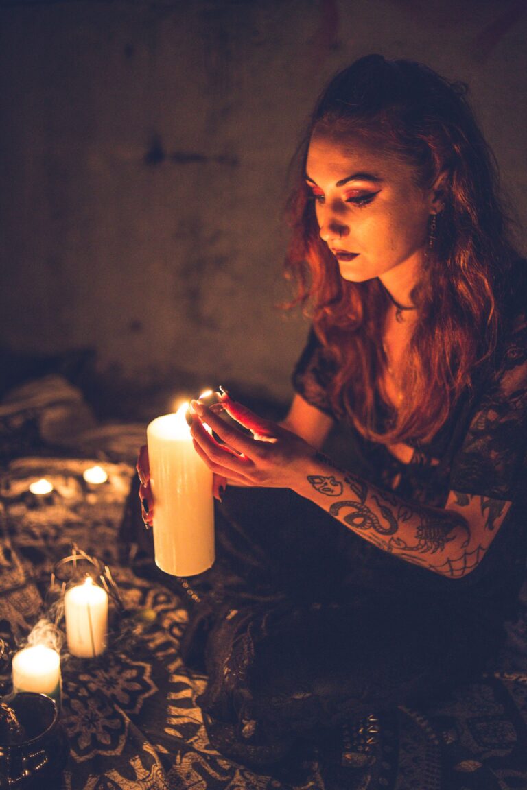 Mulher em estado contemplativo acendendo vela ritual em ambiente escuro, cercada por outras velas acesas no chão