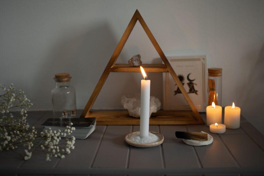 Altar de proteção montado em casa com vela acesa, cristais, tarô e flores secas sob estrutura triangular de madeira