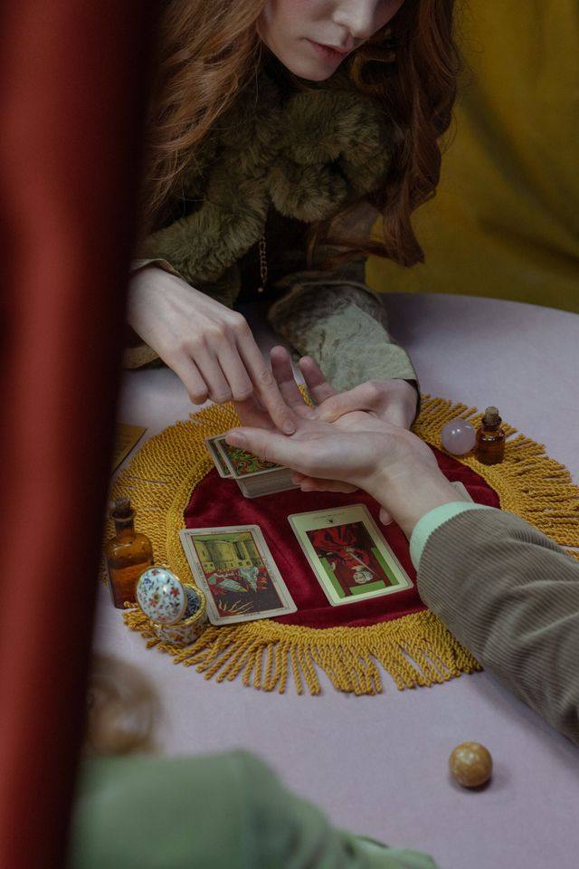 Quiromante lendo as linhas da mão de uma consulente, com cartas de tarô e frascos ritualísticos sobre a mesa